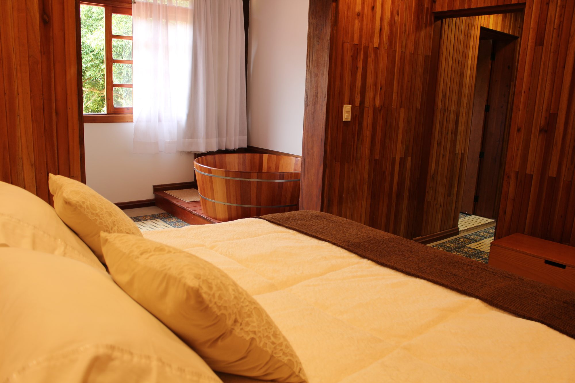 Suíte Jacarandá — ofurô ao lado da cama com janela para a mata